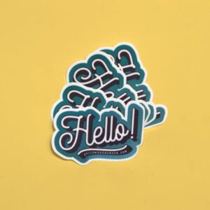 Sticker printing by YellowDog Denver: die cut blue, white and black sticker on yellow background with the word "Hello!" in cursive letters.
