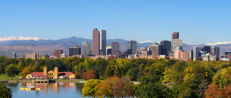 Skyline of Denver downtown with City Park lake in the foreground and front range mountains behind.