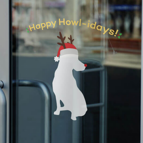 Window decal on glass door with white dog silhouette wearing reindeer ears, a red nose and Santa hat below the words "Happy Howl-idays!" bordered by holly