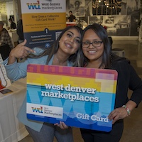 Two women pose with an oversized West Denver Marketplaces Gift Card.