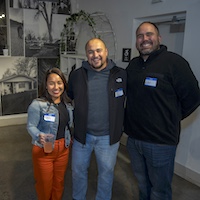 A group of three poses in front of a black-and-white indoor mural.
