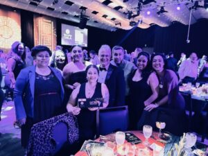 Eight adults in formalwear standing behind a banquet table.