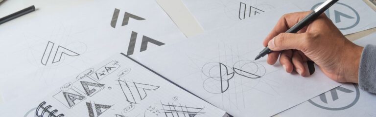 Close up image of a hand designing a logo on a sheets of paper containing multiple A-shaped logos