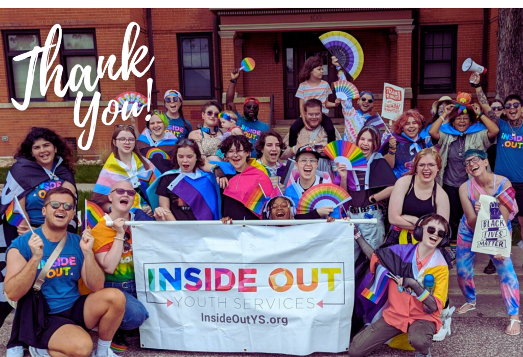 A group of 20+ children and young adults smiling with an "Inside Out Youth Services" banner in front of a bright building. Some individuals are waving or wearing Pride flags. Others are holding rainbow-colored paper fans. Many are wearing blue t-shirts with the Inside Out logo.