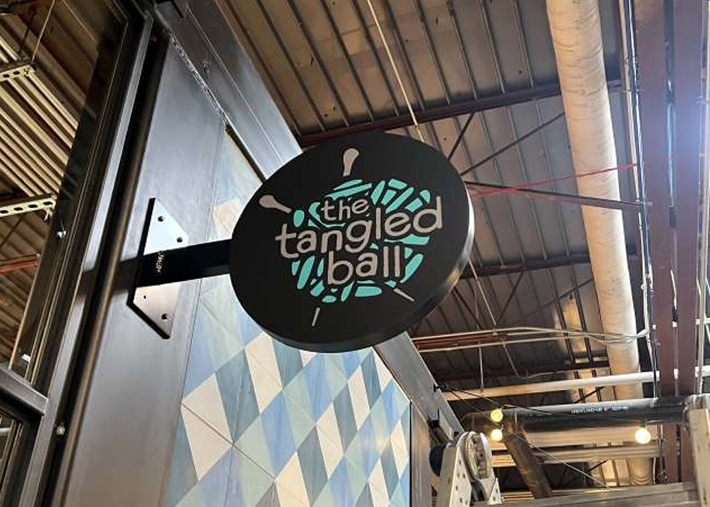 "the tangled ball" business name and logo on a circular, three-dimensional sign affixed to a wall.