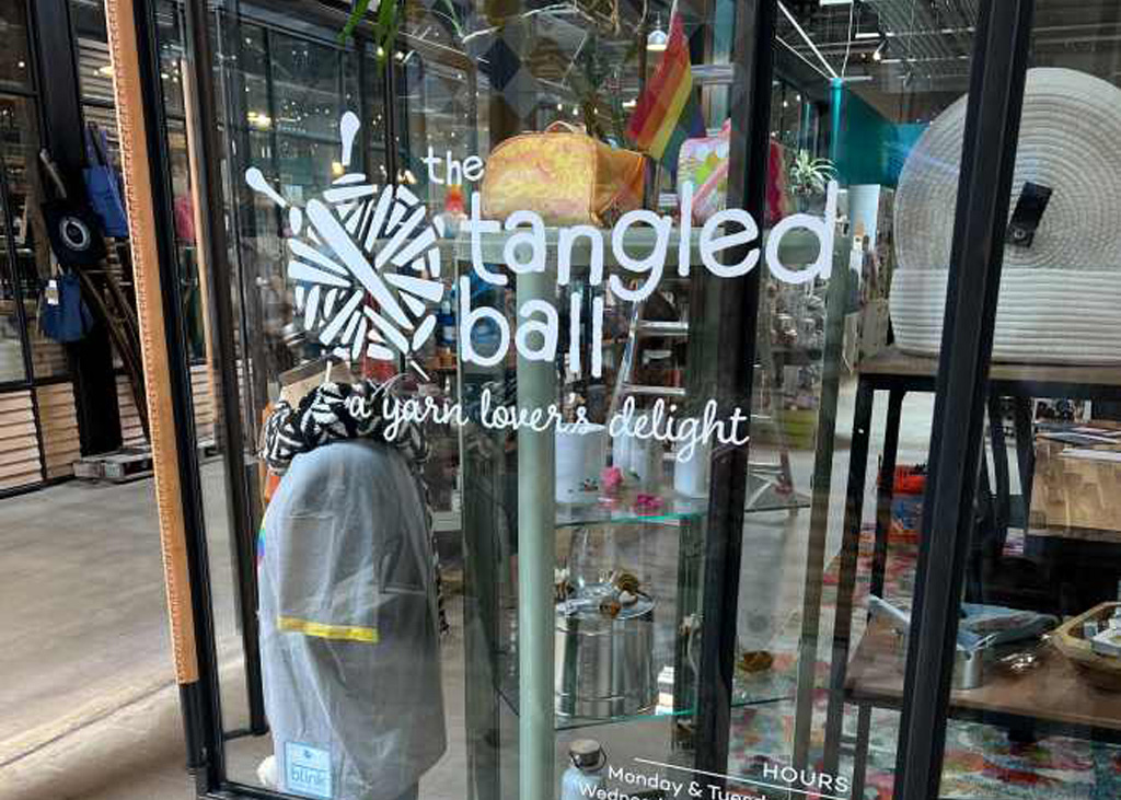 whit vinyl lettering, designed and printed by YellowDog, on a glass wall  depicts the tangled ball logo, name and tagline (a yarn lover's delight)
