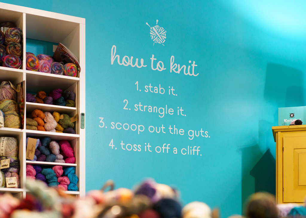 White vinyl lettering, designed and printed by YellowDog reads: "how to knit - 1. stab it. 2. strangle it. 3. scoop out the guts. 4. toss it off a cliff."