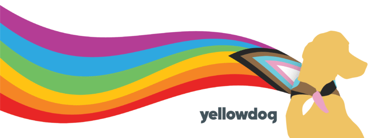 YellowDog logo mark (the silhouette of a yellow labrador sitting up, looking off to the right) is wearing a long rainbow bandana cape depicting the Pride flag, flowing across the frame as if blowing in the breeze.